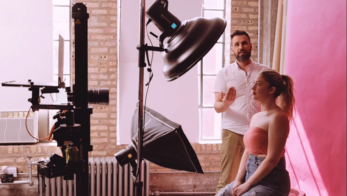 Photographer and model on set with large softbox and key light positioned for portrait photography.