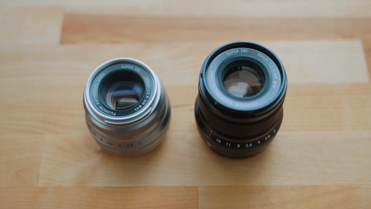 Two vintage camera lenses placed side-by-side on a wooden surface for comparison.