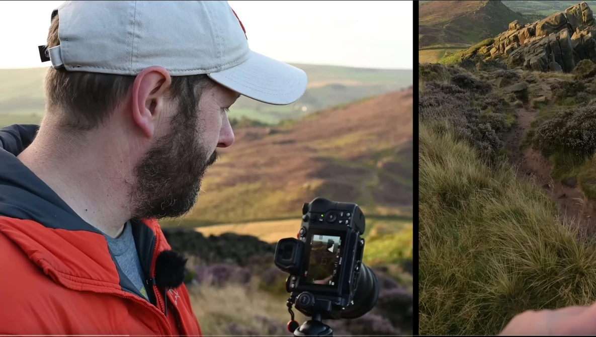 Photographer holding a camera on a tripod while framing a shot of a rocky hillside in moorland terrain.