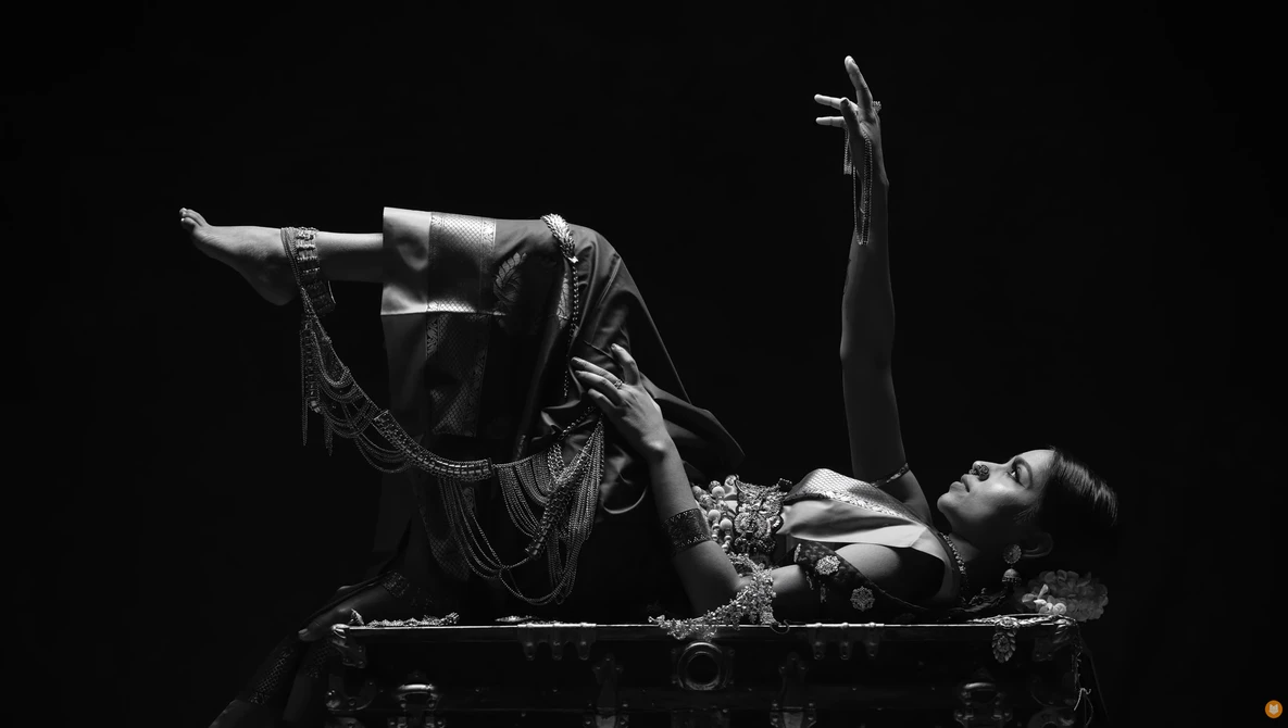 Woman in ornate costume lying on floor with arms extended, shot in dramatic high-contrast black and white.