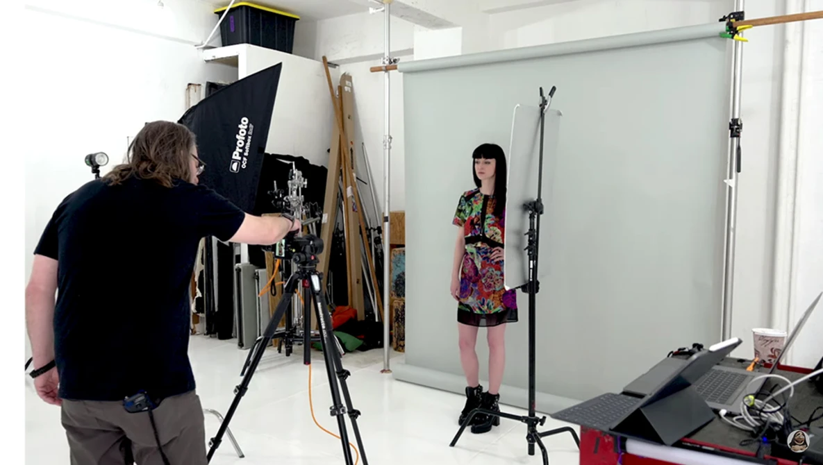 Photographer adjusting lighting setup while model poses in studio during portrait session.