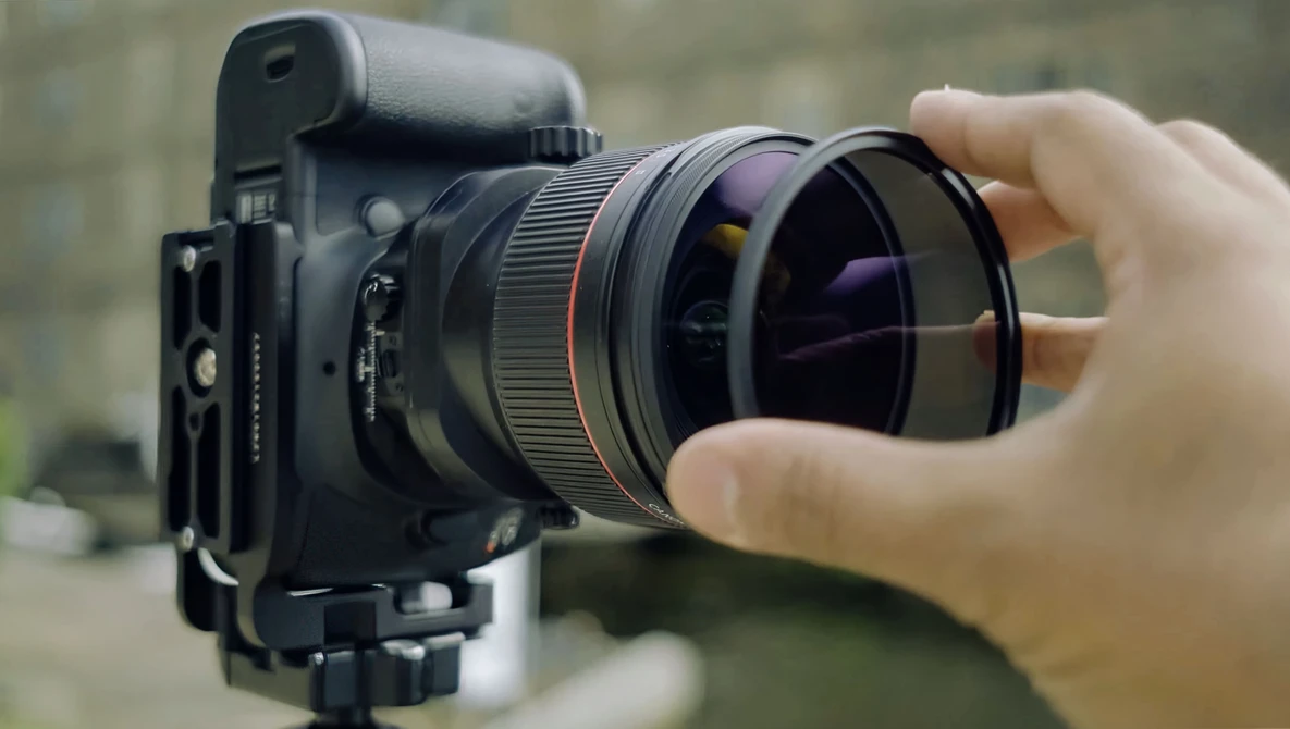 Photographer's hand adjusting a wide-angle lens on a cinema camera mounted on a tripod.