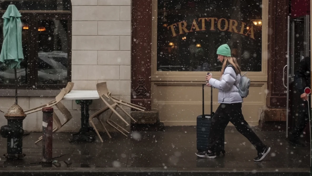 Person jogging past a trattoria storefront during heavy snowfall in an urban setting.