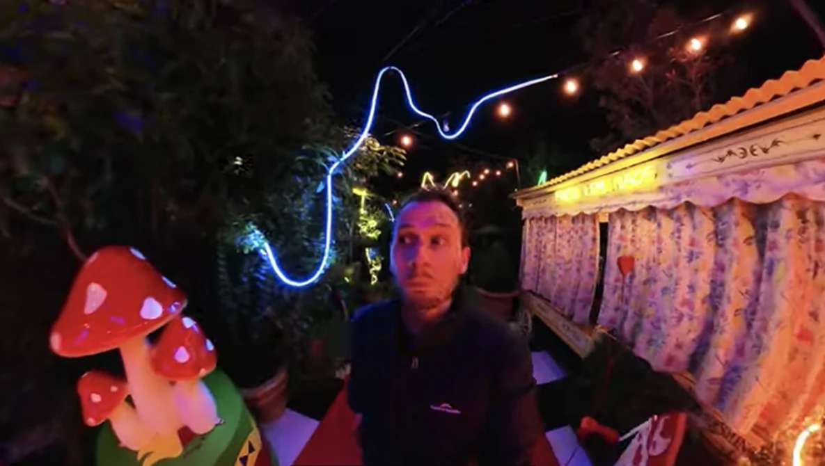 Man posing with neon blue lightning bolt and glowing red mushroom decorations at night.