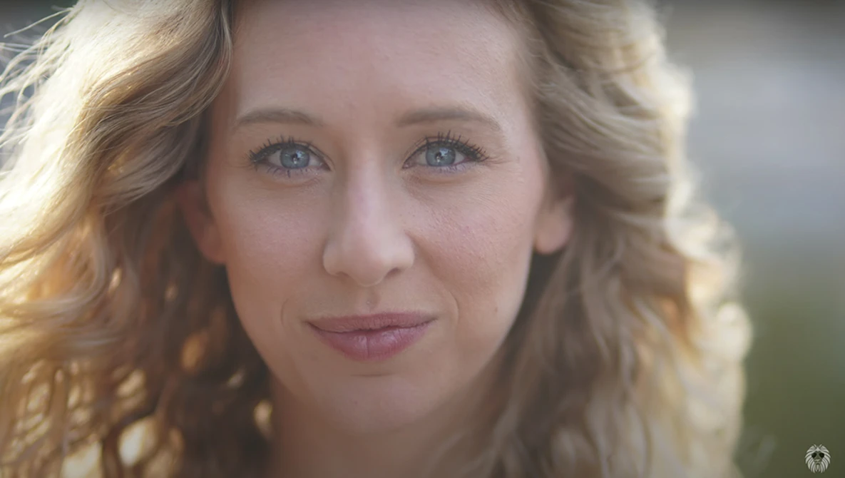 Woman with wavy blonde hair and blue eyes in golden hour portrait lighting.