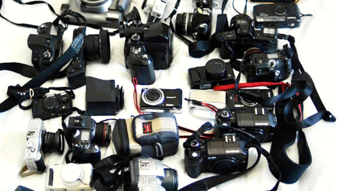 Flat lay collection of vintage film cameras and photography equipment arranged on white background.