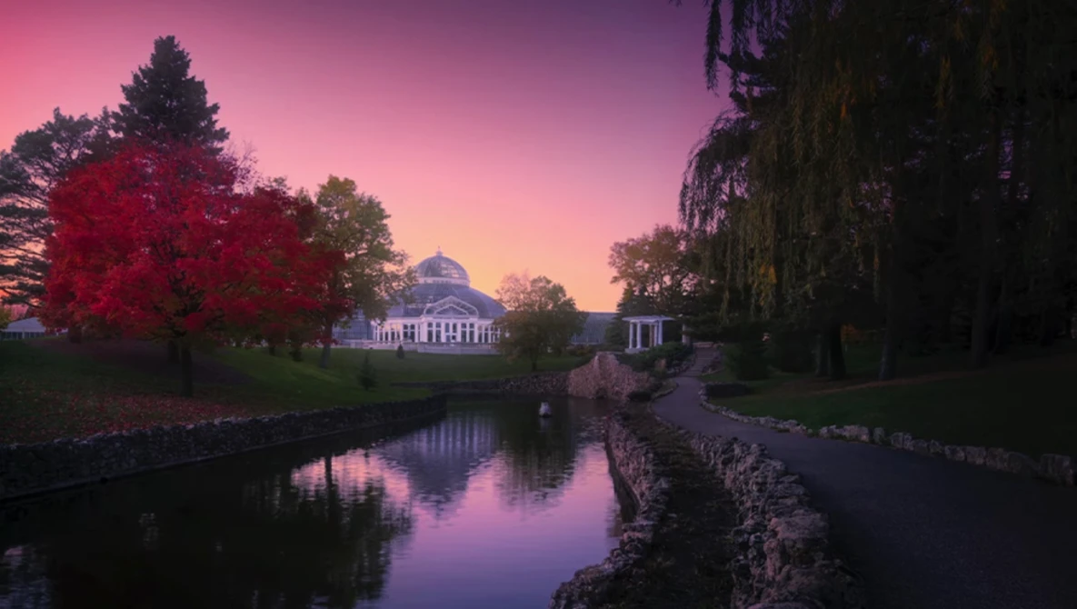 Classical white building reflected in still water at twilight, framed by autumn trees and weeping willow.