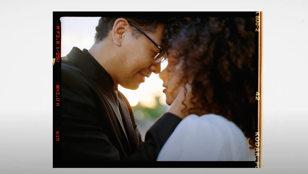 Two people facing each other in close proximity during golden hour, one wearing glasses and a black jacket.