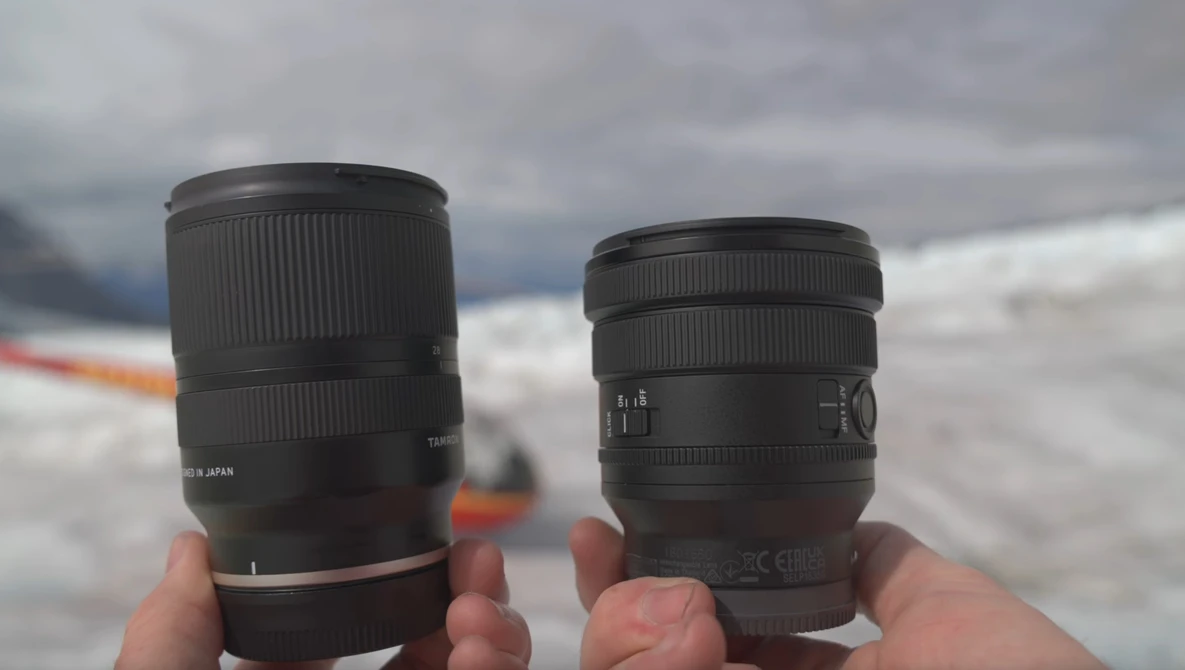 Two telephoto lenses held in hands against a snowy mountain landscape.