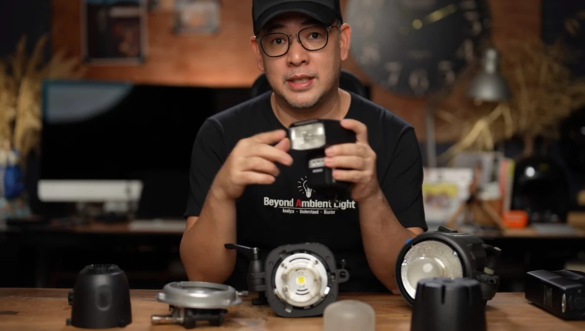 Photographer holding a small LED light modifier while examining studio lighting equipment on a table.