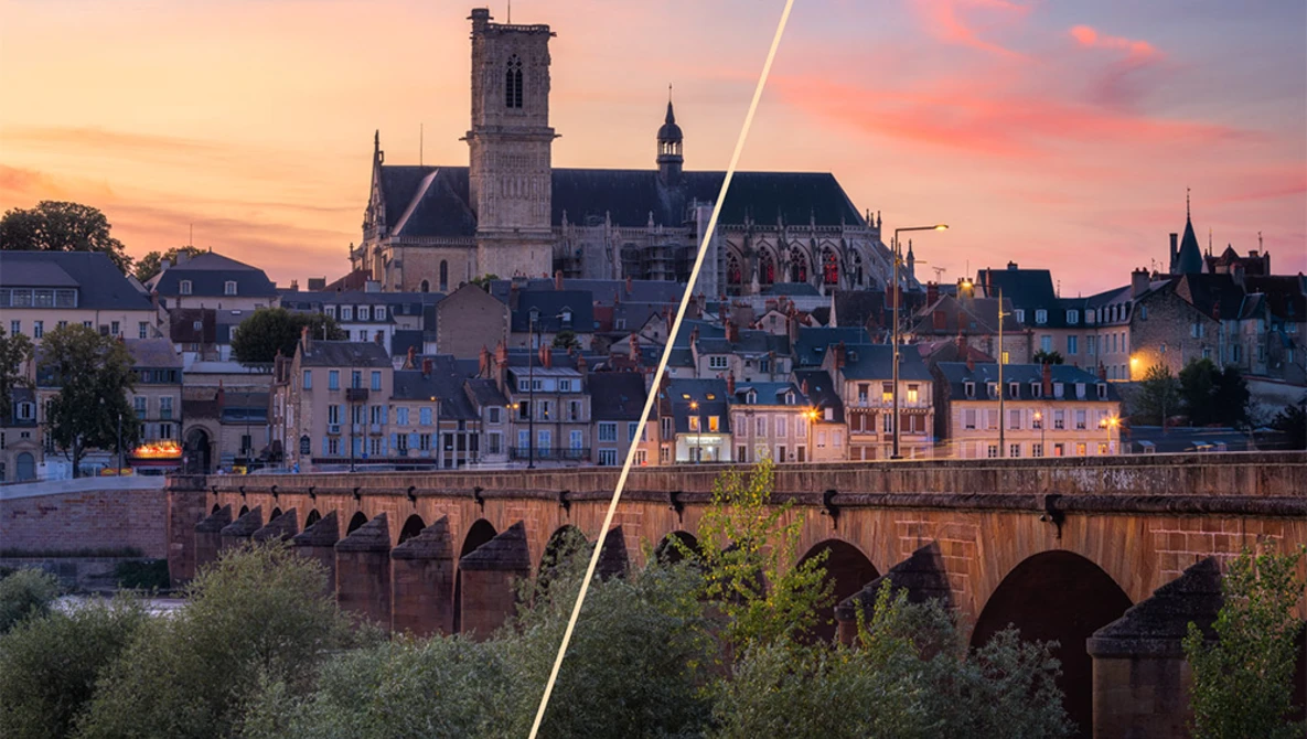 Medieval riverside town at sunset with stone bridge and cathedral spire illuminated by golden and pink sky.