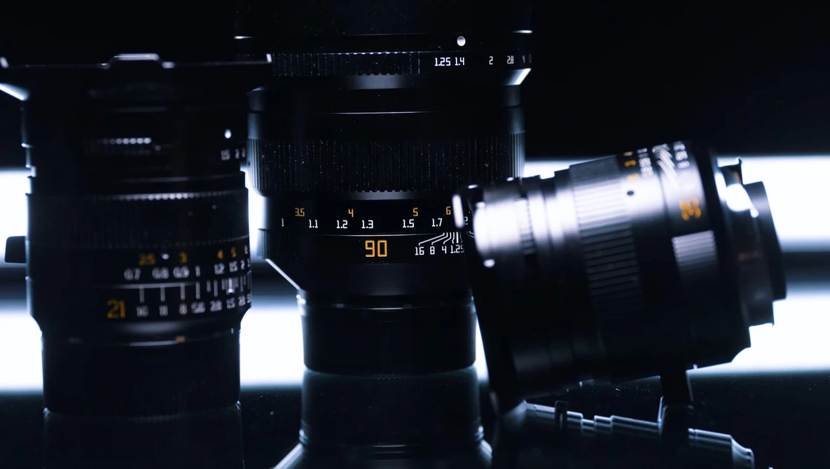 Collection of camera lenses arranged against backlit white background, showing focus rings and aperture markings.