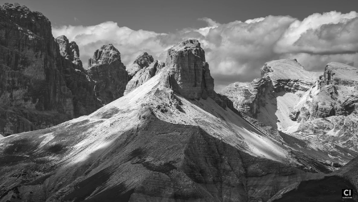 Dramatic mountain peaks with snow and exposed rock formations under a cloudy sky.