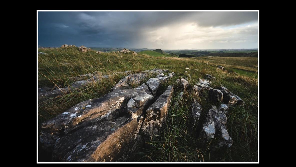 Weathered rock outcrop in grassland with dramatic cloudy sky and distant hills.