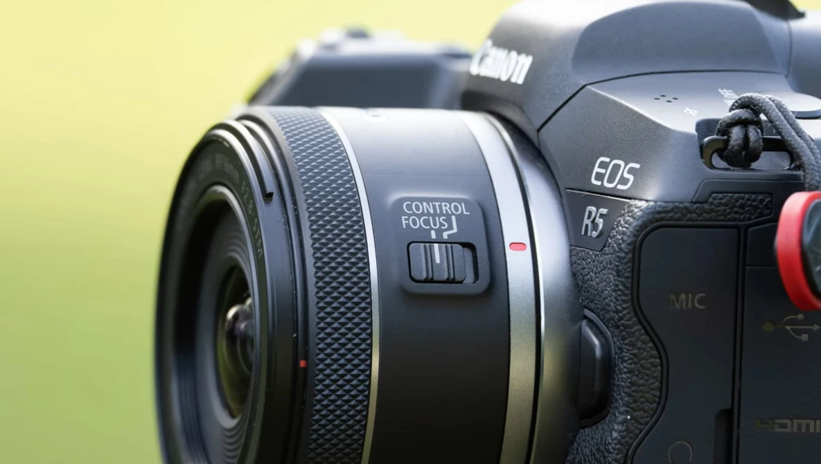 Canon EOS R5 mirrorless camera with RF-mount lens against a soft yellow-green background.