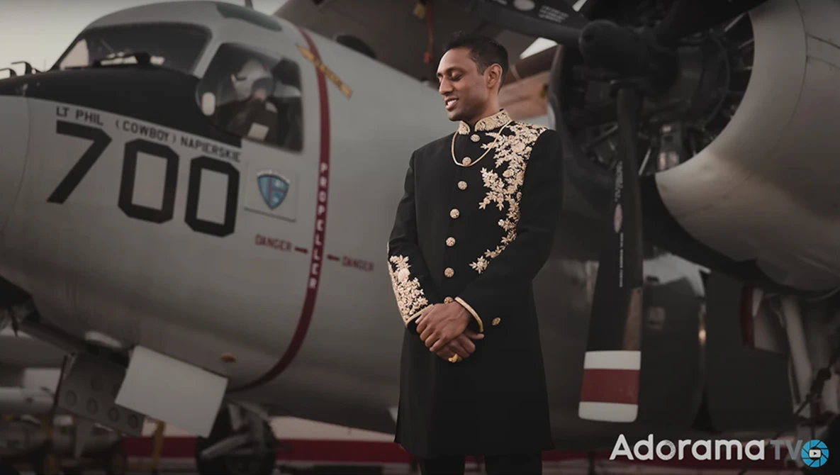 Man in ornate black military dress uniform standing beside aircraft fuselage numbered 700.