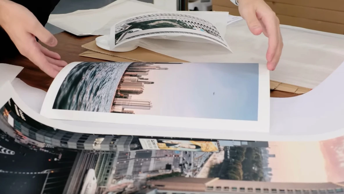 Hands arranging printed photo prints on a wooden table, including landscape and architectural images.