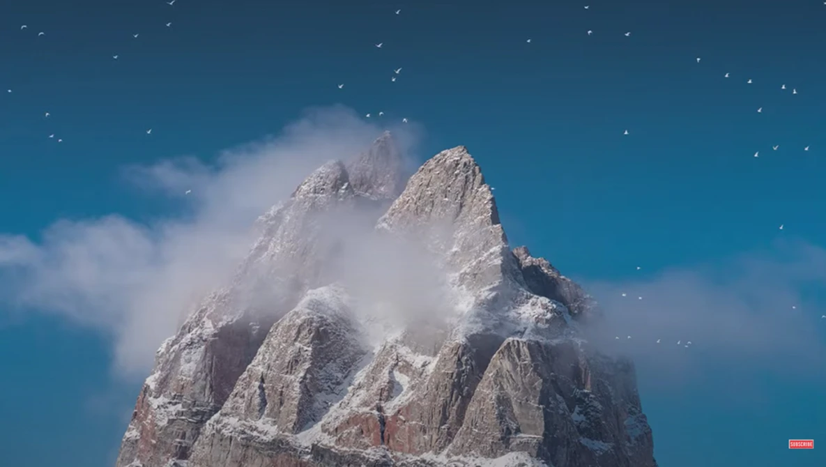 Snow-covered mountain peak against deep blue sky with white clouds and stars.