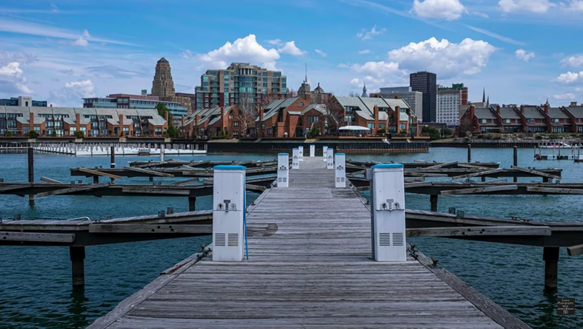 White wooden pier extending toward a waterfront city skyline with historic and modern architecture.