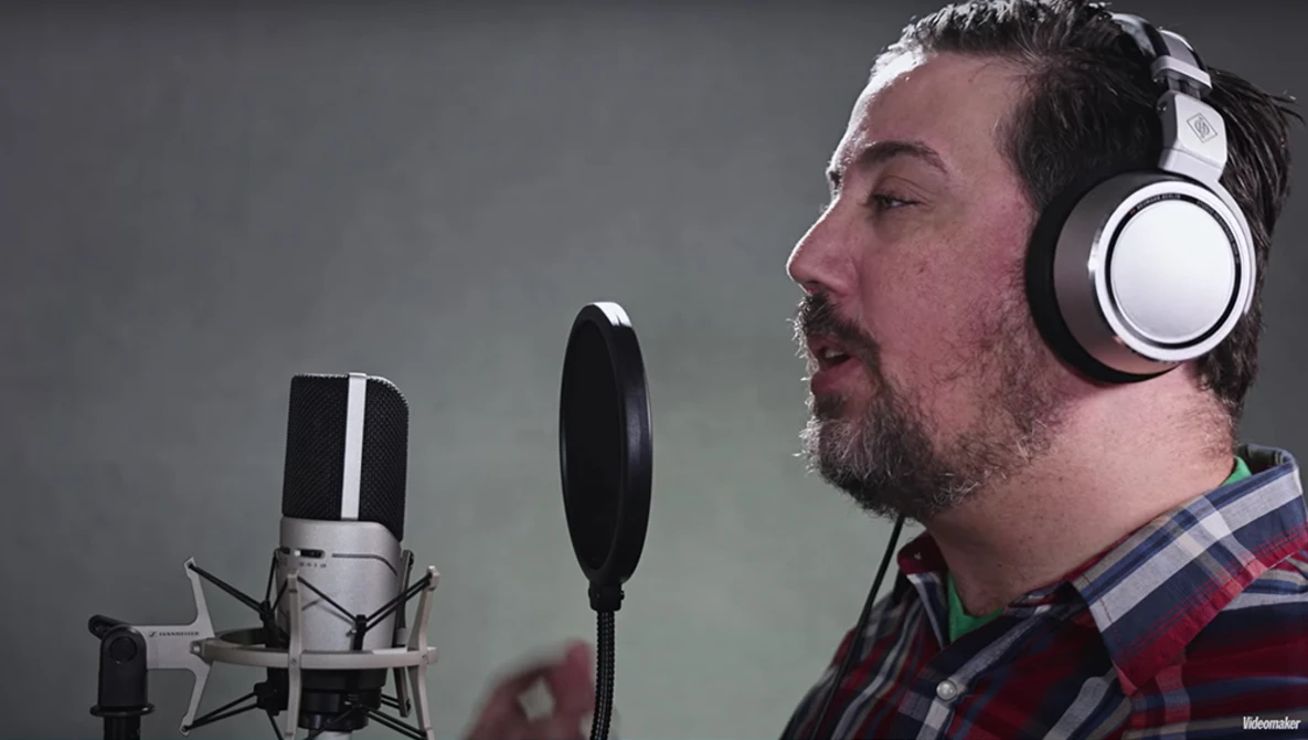 Male voice actor wearing headphones while recording into a large-diaphragm condenser microphone with pop filter.