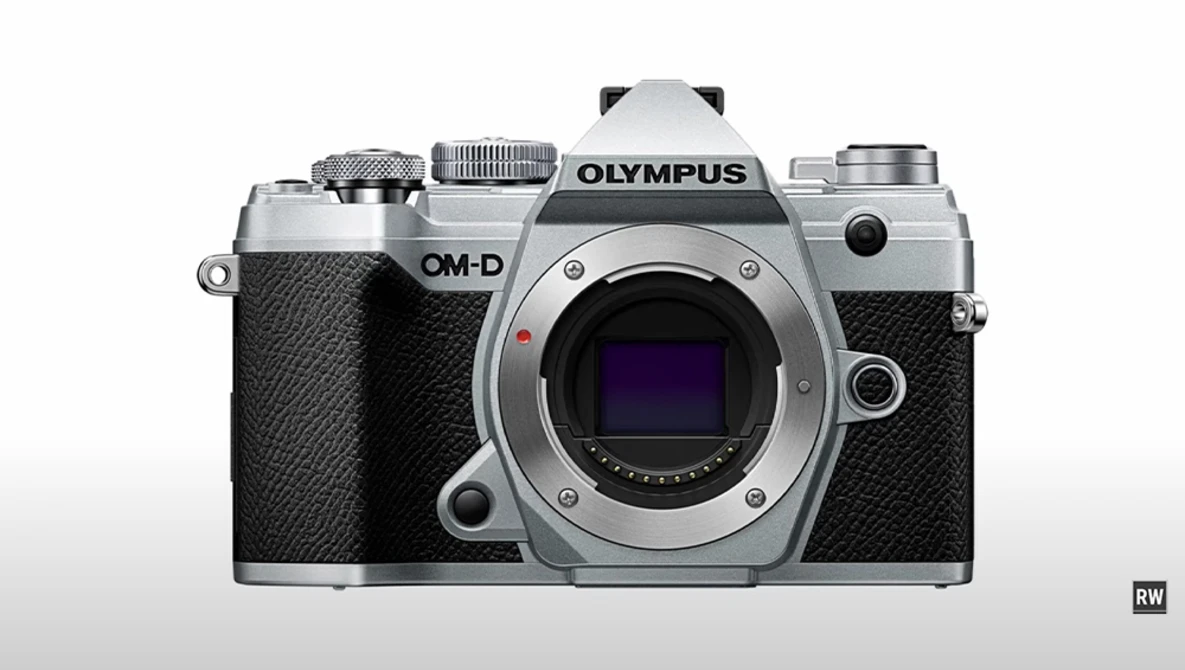 Olympus OM-D mirrorless camera body shown from front, silver and black finish with visible sensor and controls.