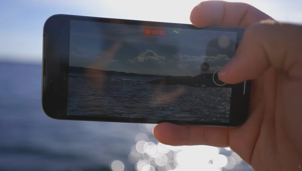 Hand holding smartphone recording video of ocean and sky at sunset or sunrise.