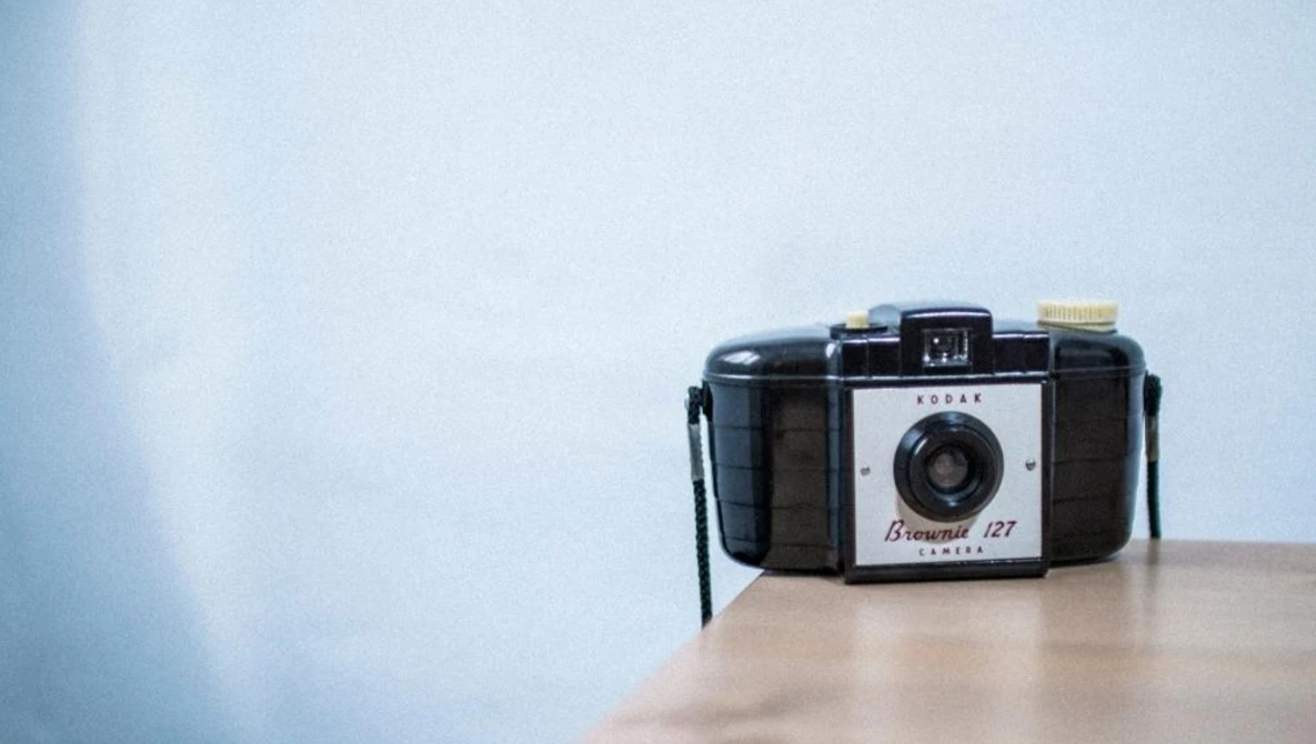 Vintage folding camera with white and black body positioned on a wooden surface against a soft blue wall.