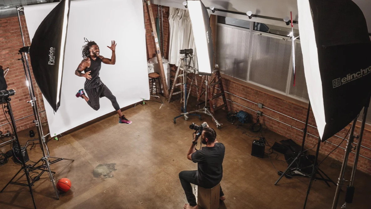 Photographer shooting a dynamic athletic portrait in a studio with softbox lighting and brick walls.
