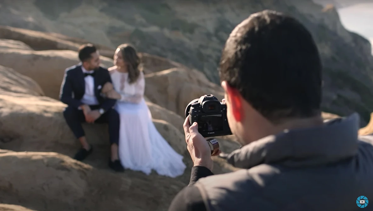 Wedding photographer shooting bride and groom posing on rocky terrain during golden hour.