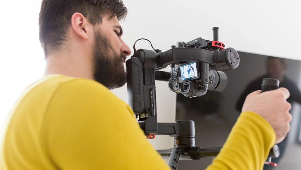 Videographer in yellow shirt operating a cinema camera mounted on a stabilizing rig.