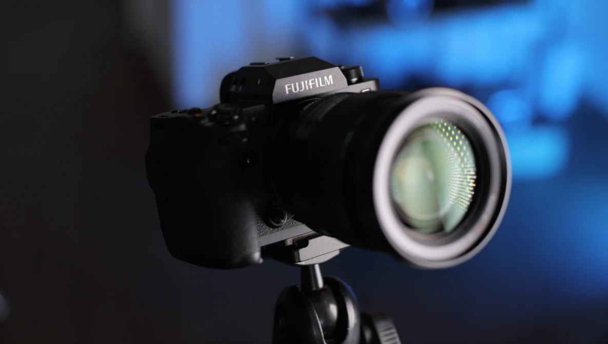 Fujifilm camera mounted on tripod with ring light attached, photographed against blurred blue background.