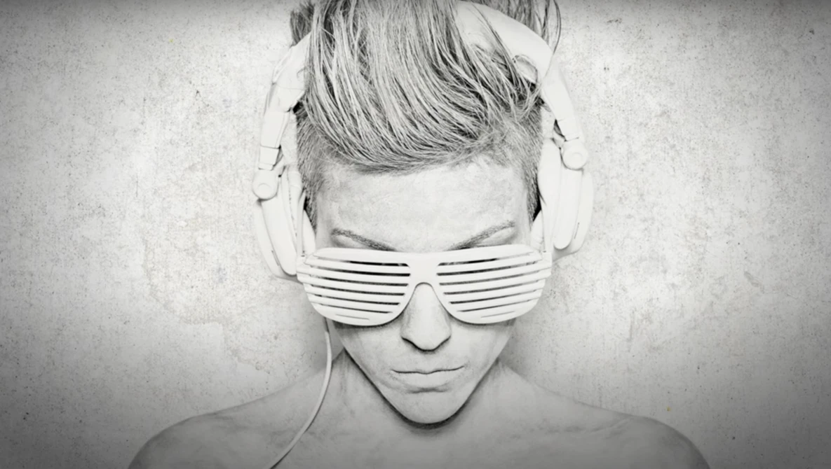 Monochrome portrait of person wearing slotted sunglasses and headphones with shaved undercut hairstyle.