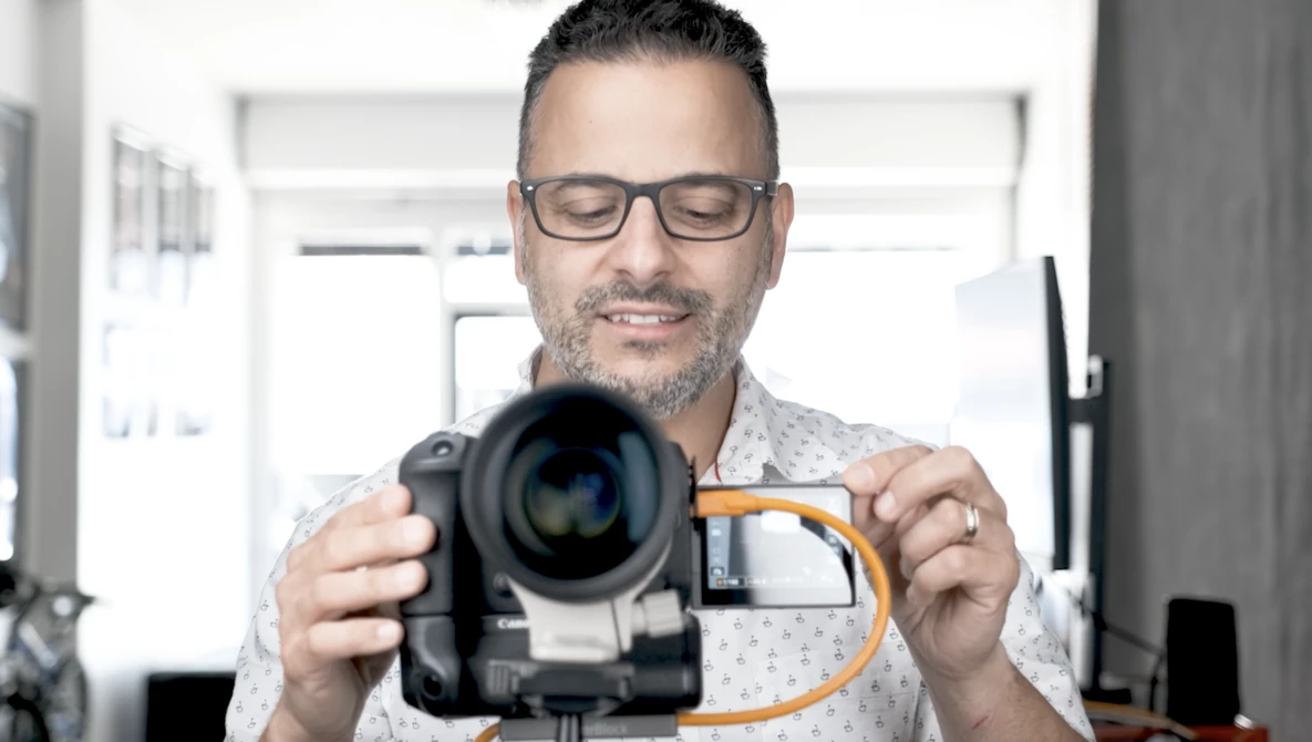 Photographer wearing glasses holding a video camera with an orange lens adapter attached.
