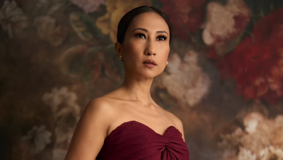 Woman in burgundy strapless dress against ornate floral backdrop.