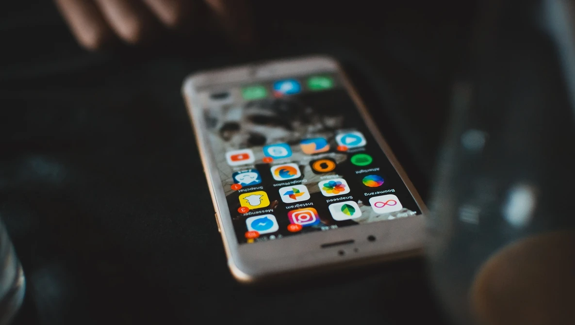 Smartphone with colorful app icons displayed on screen, held at an angle in dim lighting.