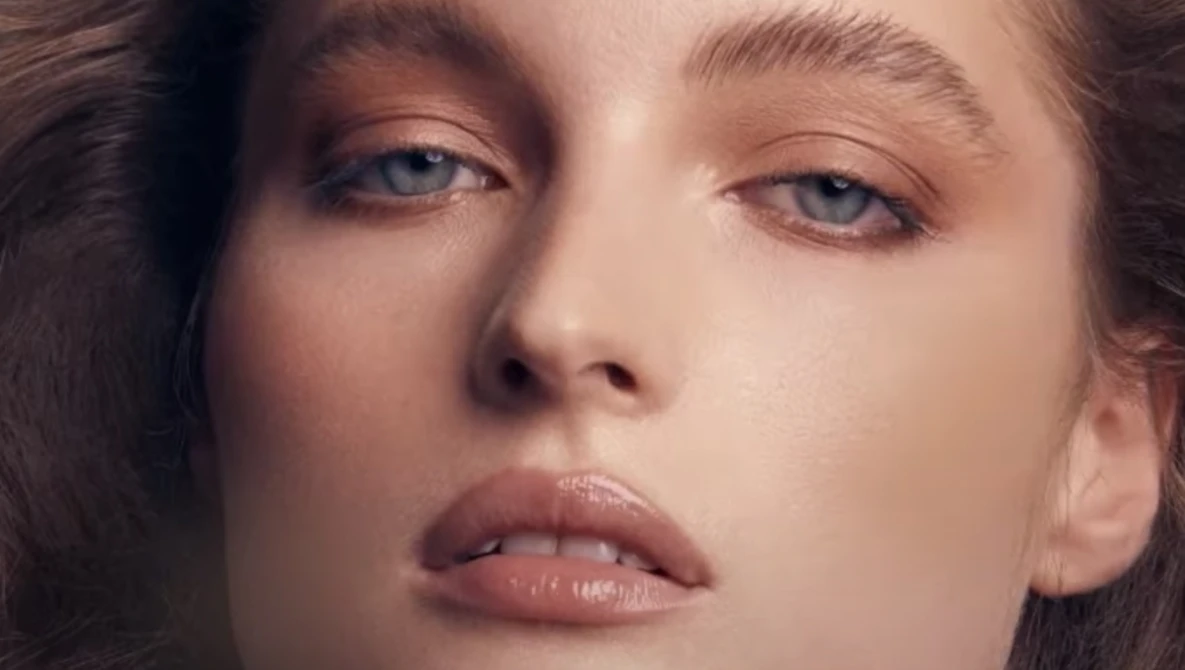 Close-up portrait of a woman with pale skin and blue eyes looking downward with a contemplative expression.