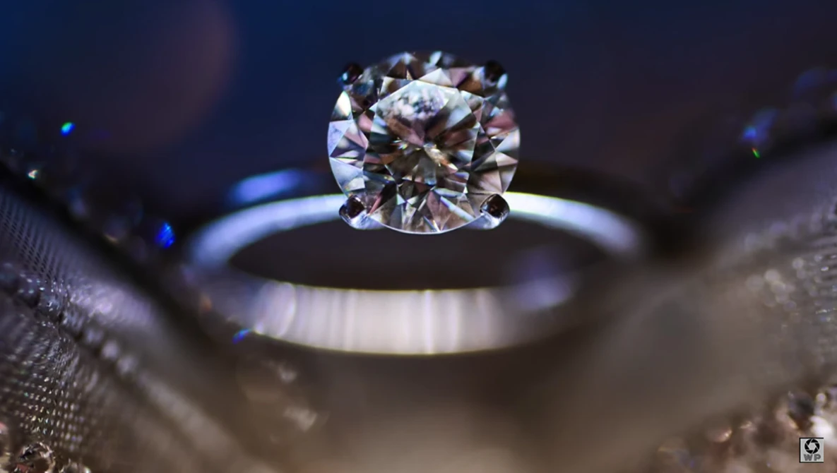 Diamond solitaire engagement ring with cushion cut stone photographed macro with shallow depth of field against dark background.