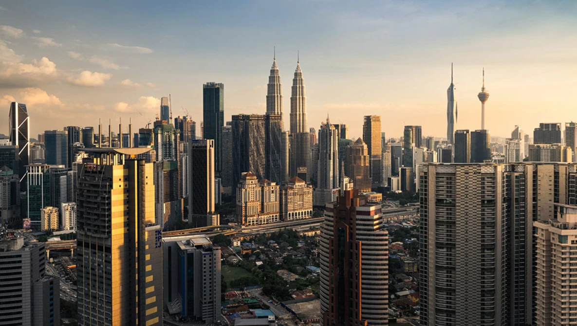 Urban skyline at golden hour with prominent twin-spire towers and residential high-rises in foreground.