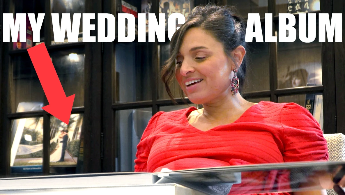 Woman in red shirt viewing wedding album pages in display case with shelving behind.