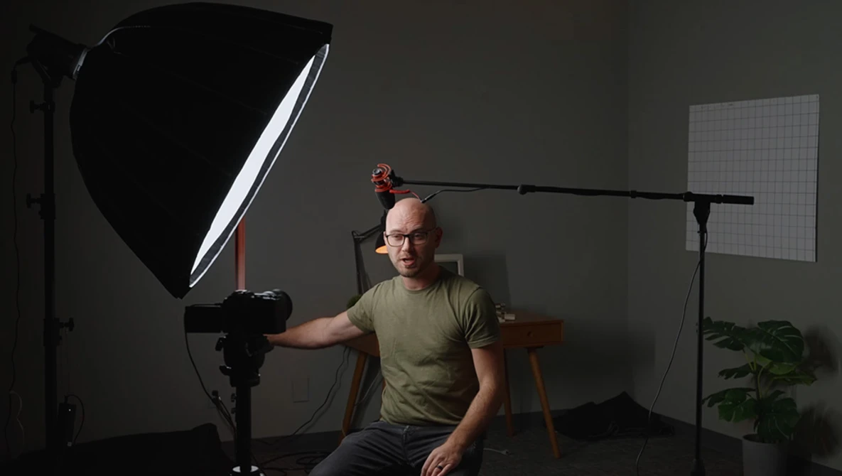 Photographer demonstrating studio lighting setup with softbox and boom arm positioned over subject.