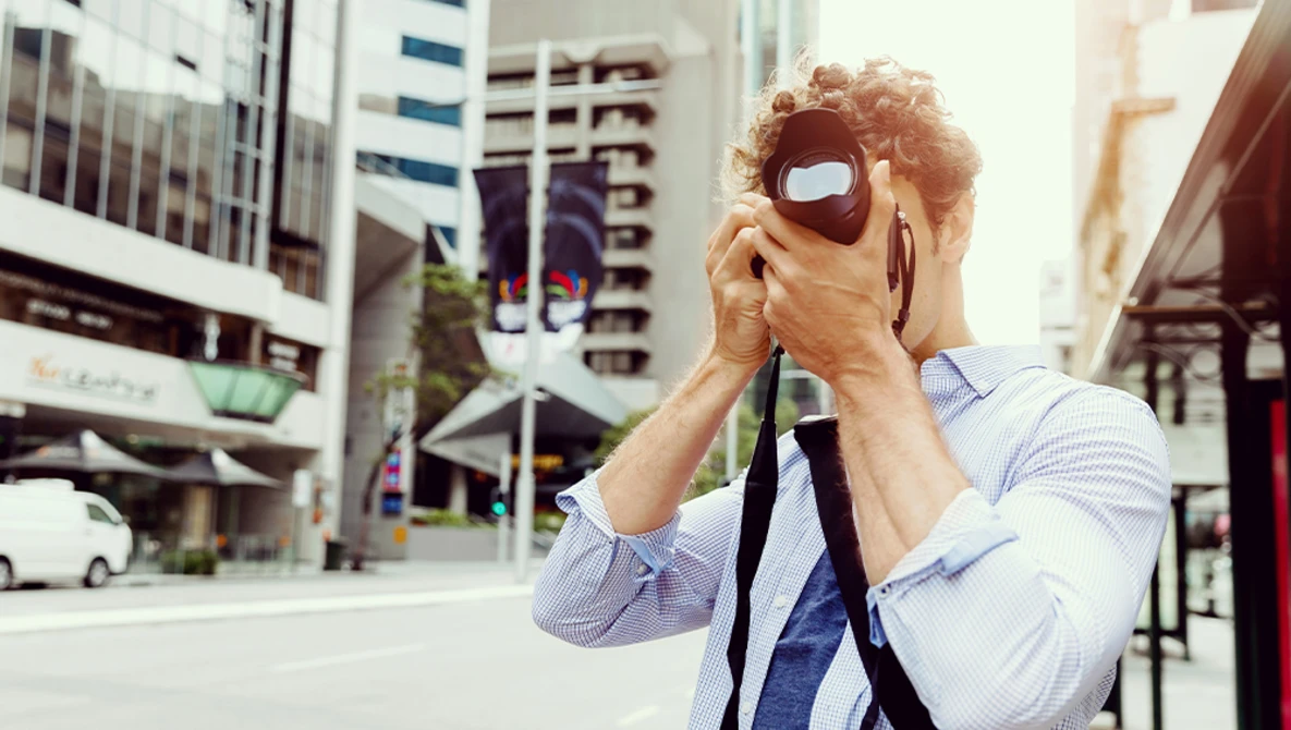 Photographer holding a mirrorless camera with red VR headset mounted on top in urban setting.