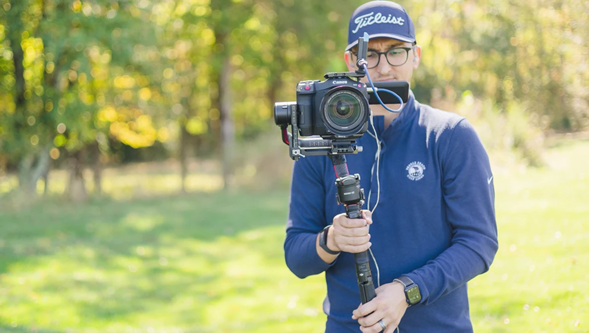 Videographer holding a cinema camera on a motorized gimbal stabilizer outdoors.