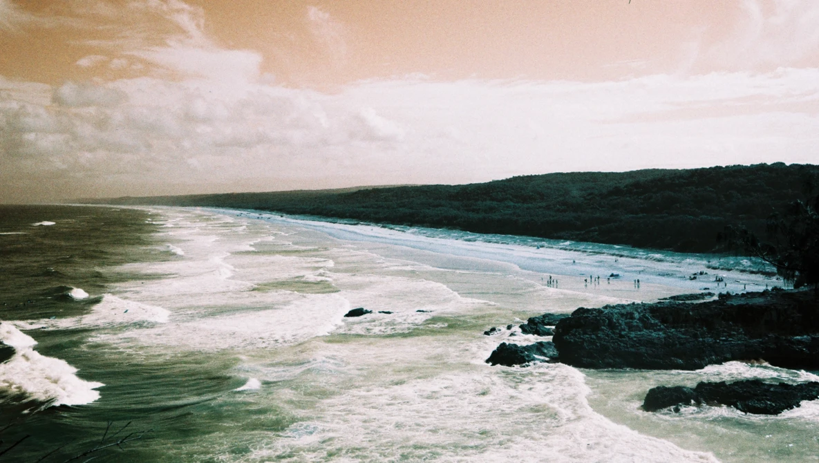 Aerial view of a dramatic coastline with turquoise waters, white sand beach, and dense forested cliffs.