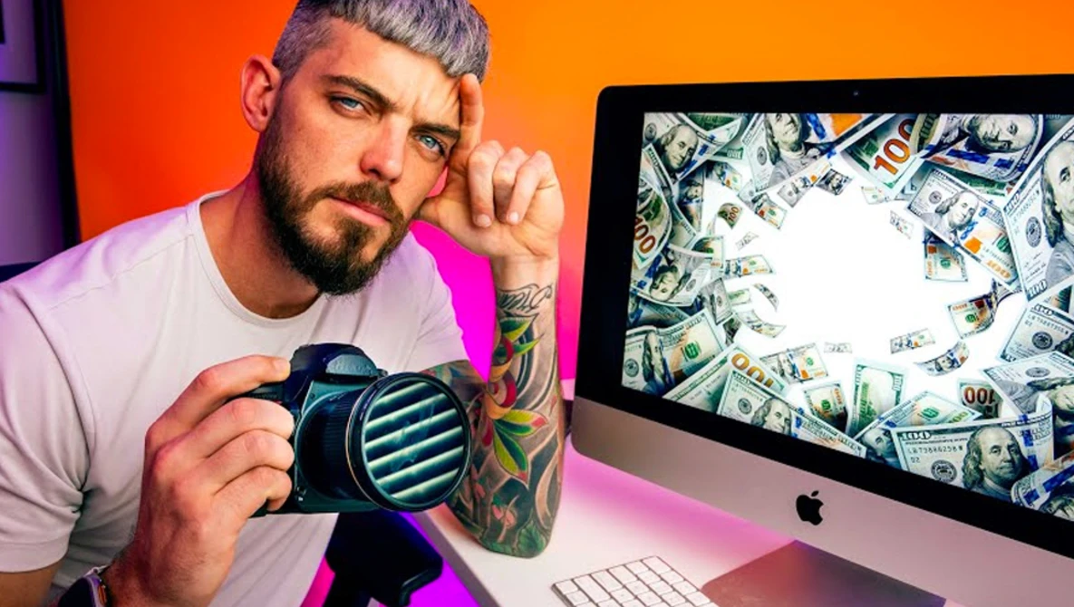 Photographer holding a mirrorless camera while looking at a desktop monitor displaying dollar bills..