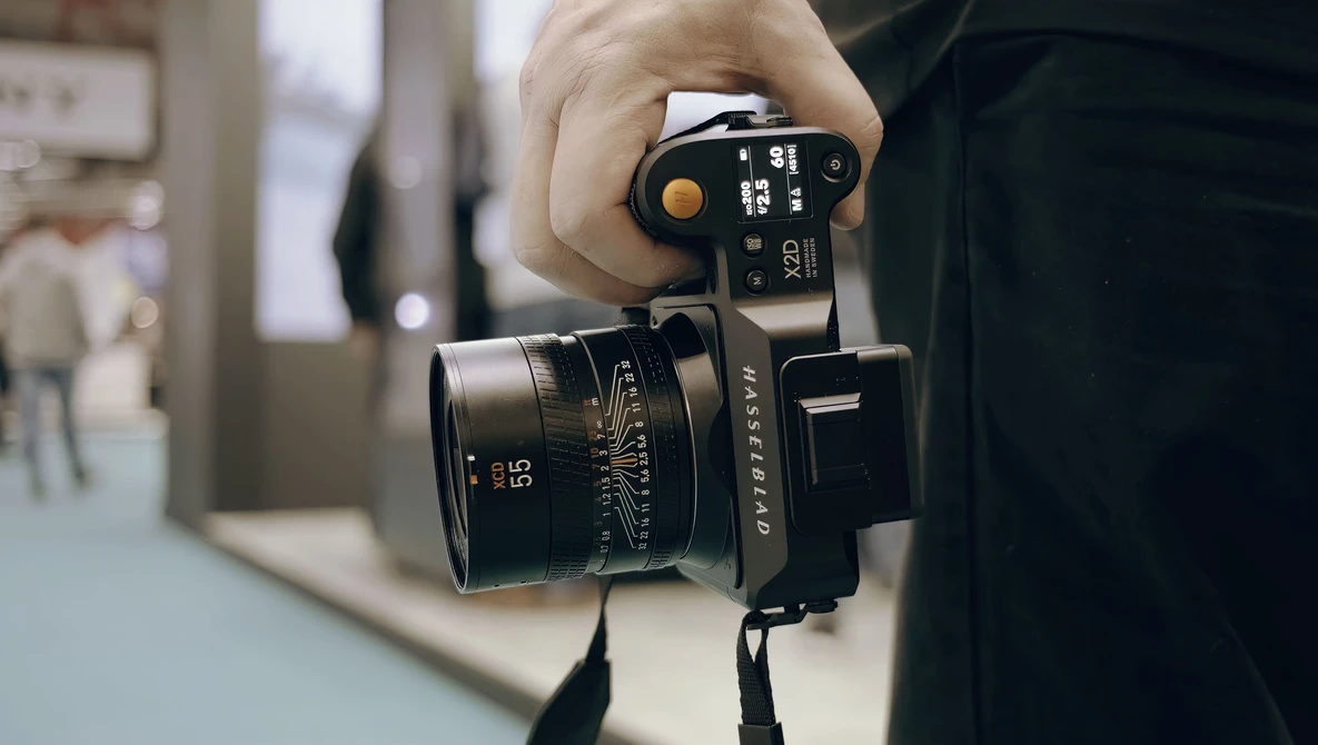 Photographer holding a film camera with a rangefinder lens, viewed from above in an indoor setting.