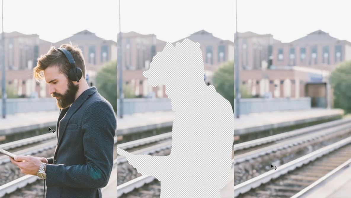 Man in blue jacket with headphones looking at phone on rooftop platform overlooking train tracks.