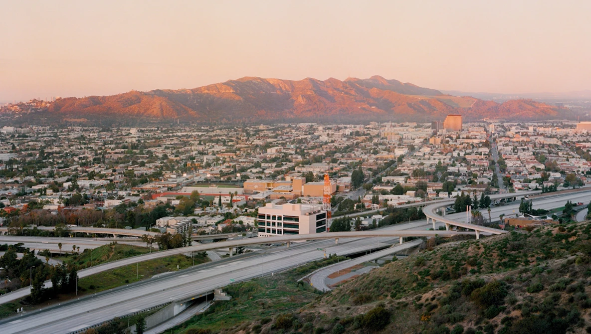 Sprawling desert city at sunset with mountains in the background and multiple highway interchanges in the foreground.