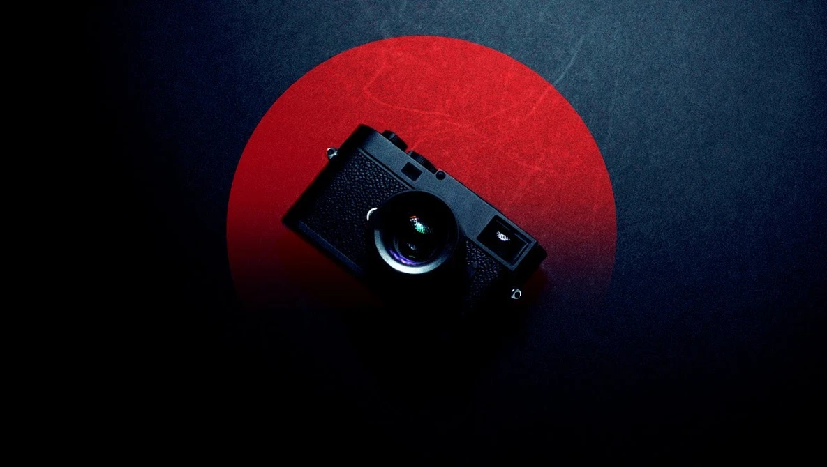 Black rangefinder camera positioned against a large red circular backdrop on dark blue background.