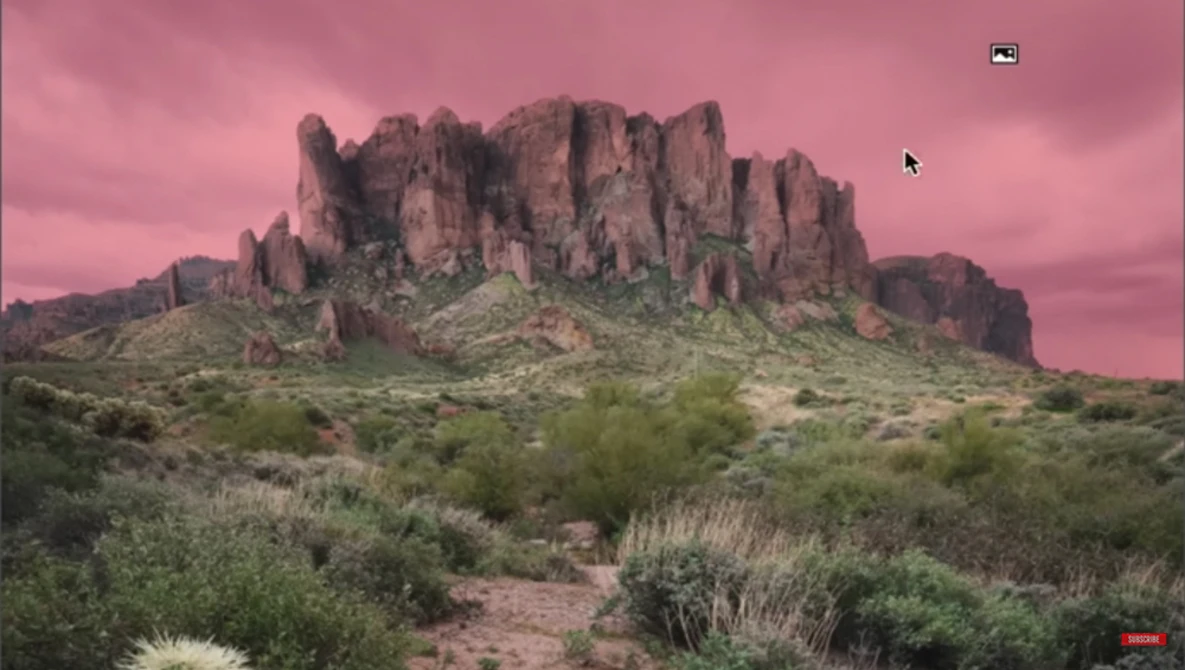 Desert mountain formation with dramatic pink sky and desert vegetation in foreground.