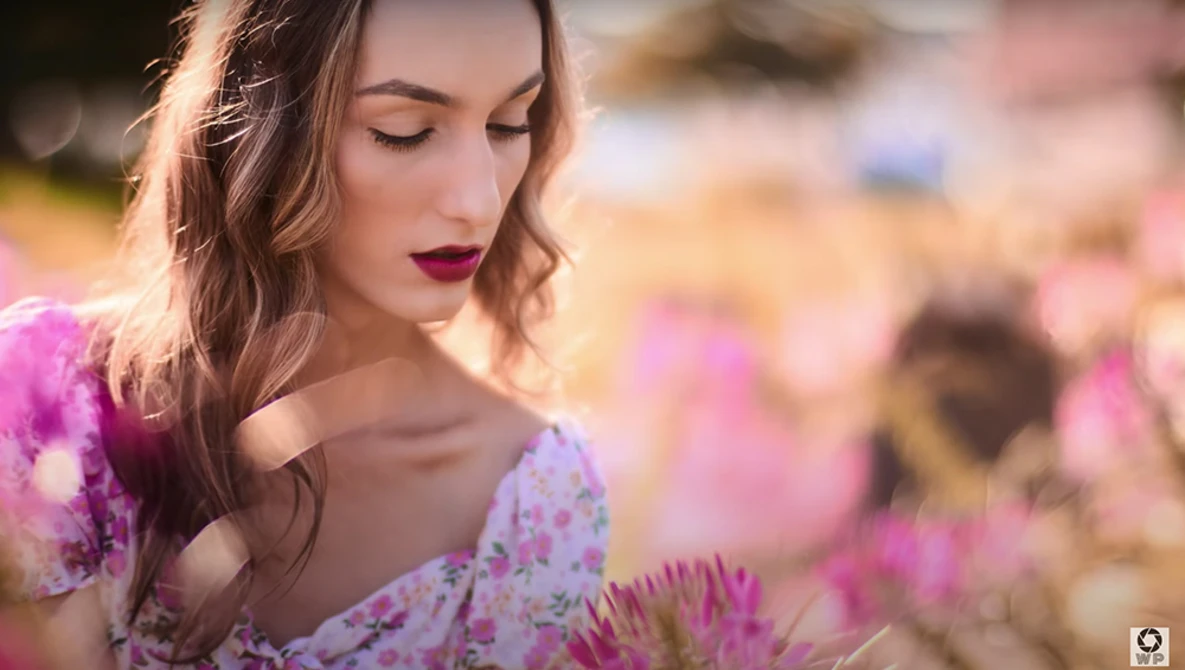 Woman in lavender floral dress among pink flowers, soft natural backlighting.